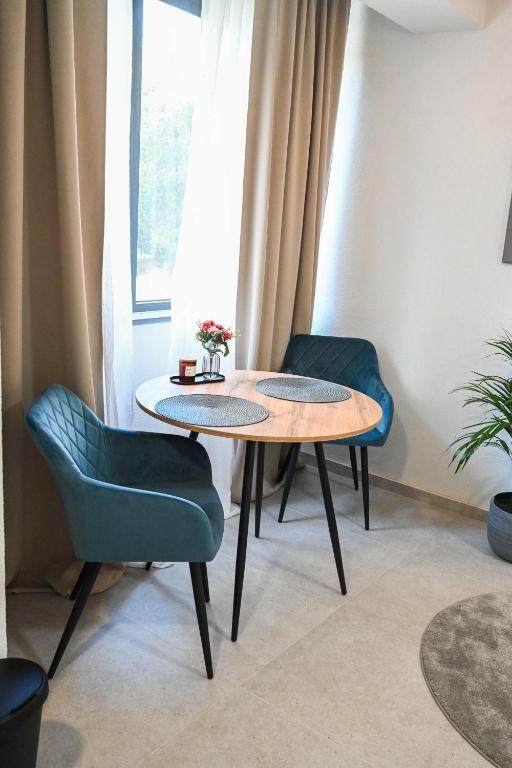 Round oak dining table with two petrol-blue velvet chairs beside a curtained window